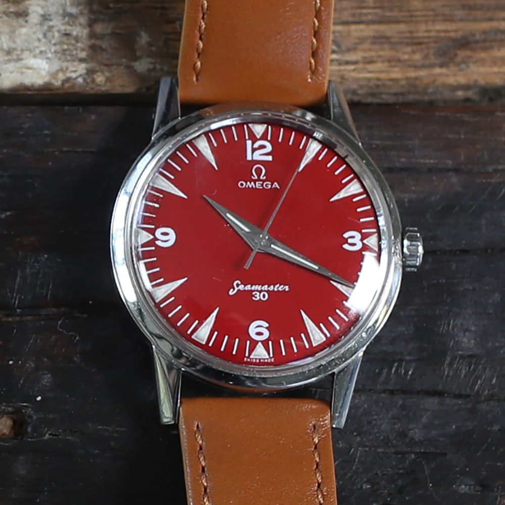 A picture of a 1947 OMEGA Seamaster with a red face and brown leather band