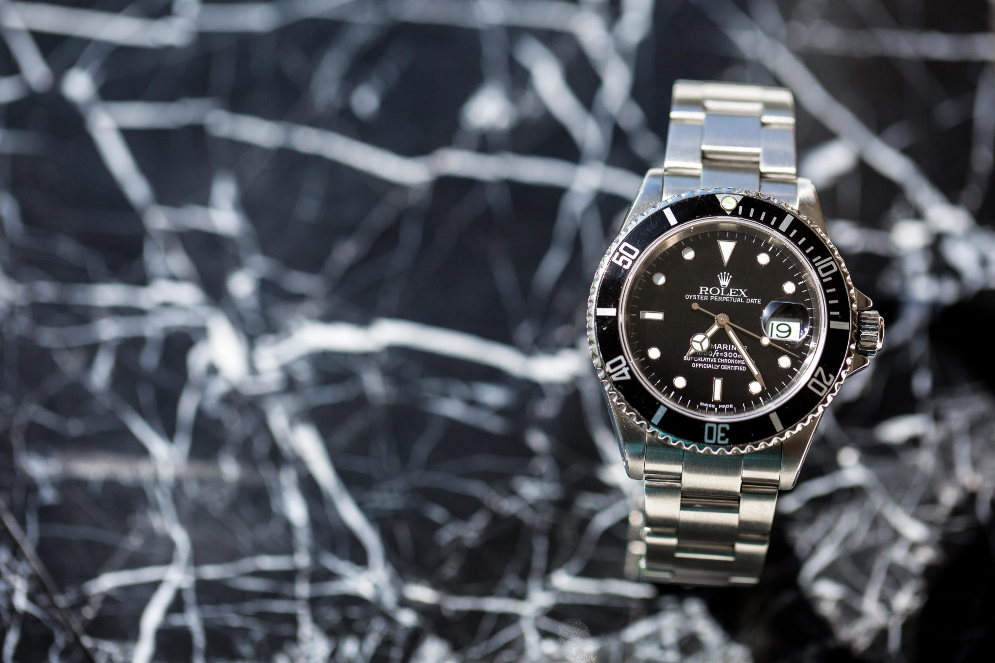 An image of a Rolex Submariner with a black dial and sitting on a piece of marble 