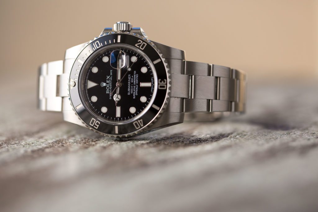 Breitling vs. Rolex: An image of a Rolex Submariner on its side with a black dial and bezel
