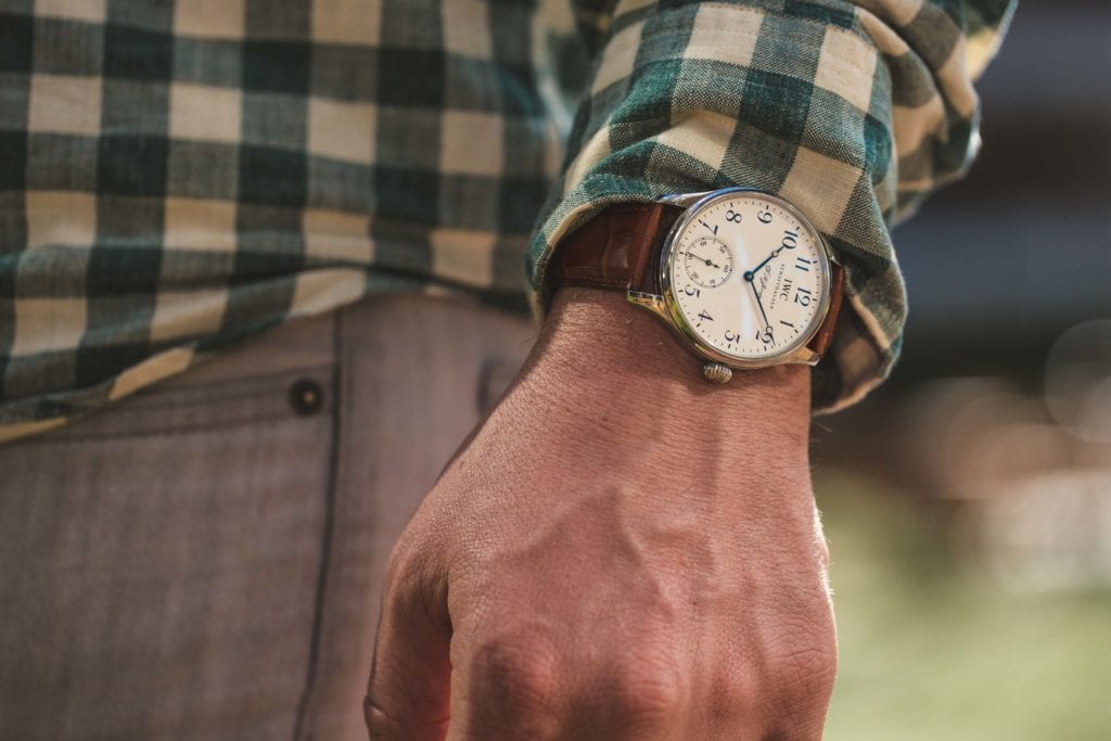 An IWC Portuguese on a man's wrist. It has a white dial and brown leather band. 